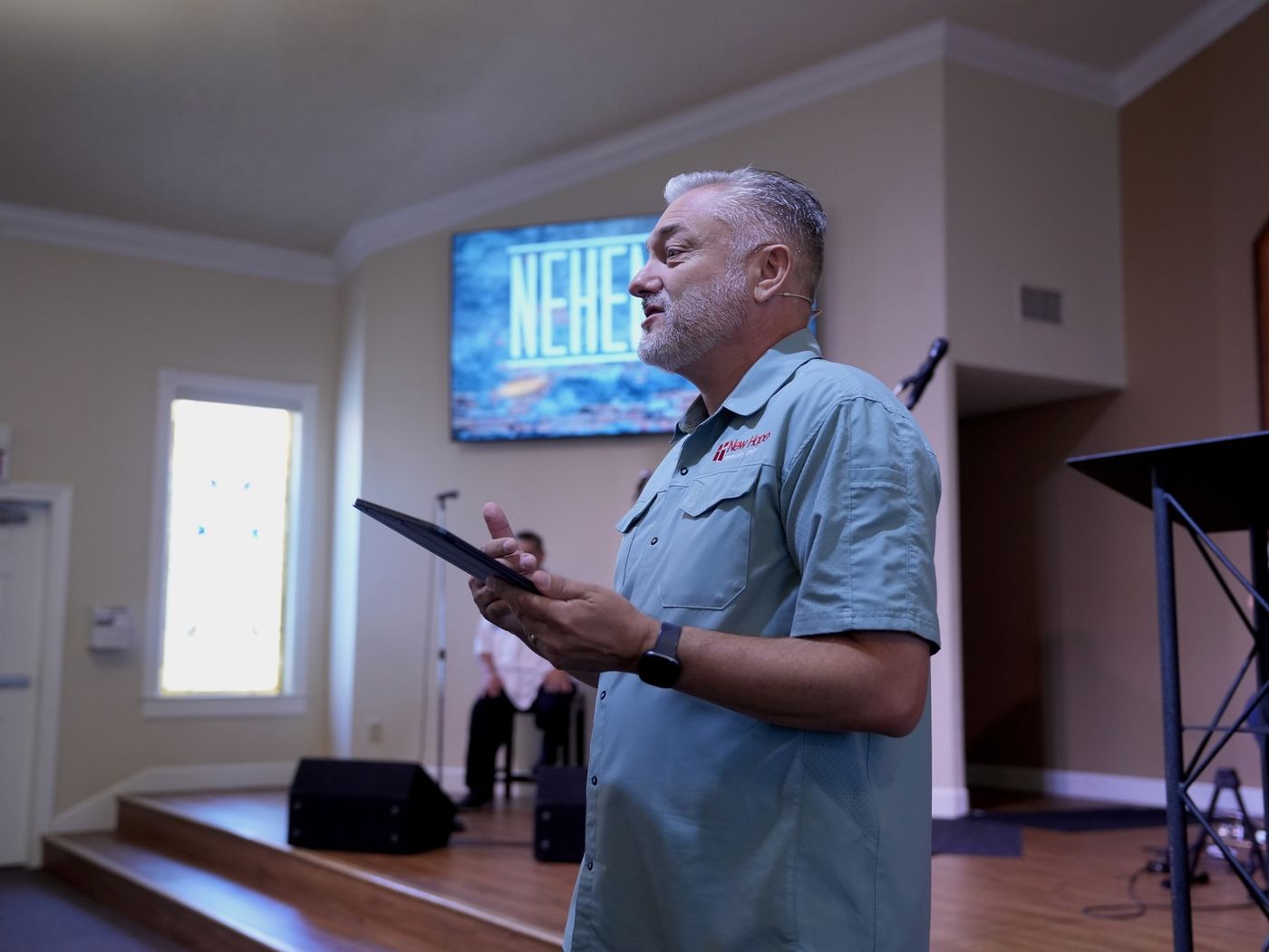 A New Hope pastor teaching from a tablet at the front of the sanctuary, a sermon-series slide on the screen behind him