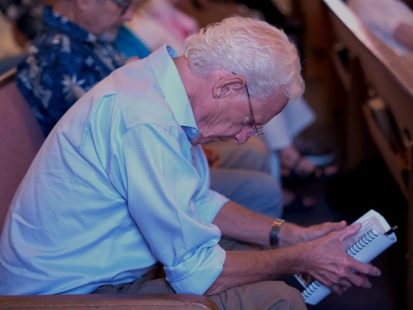 A man in a pew studying an open spiral-bound study book during a Sunday service at New Hope