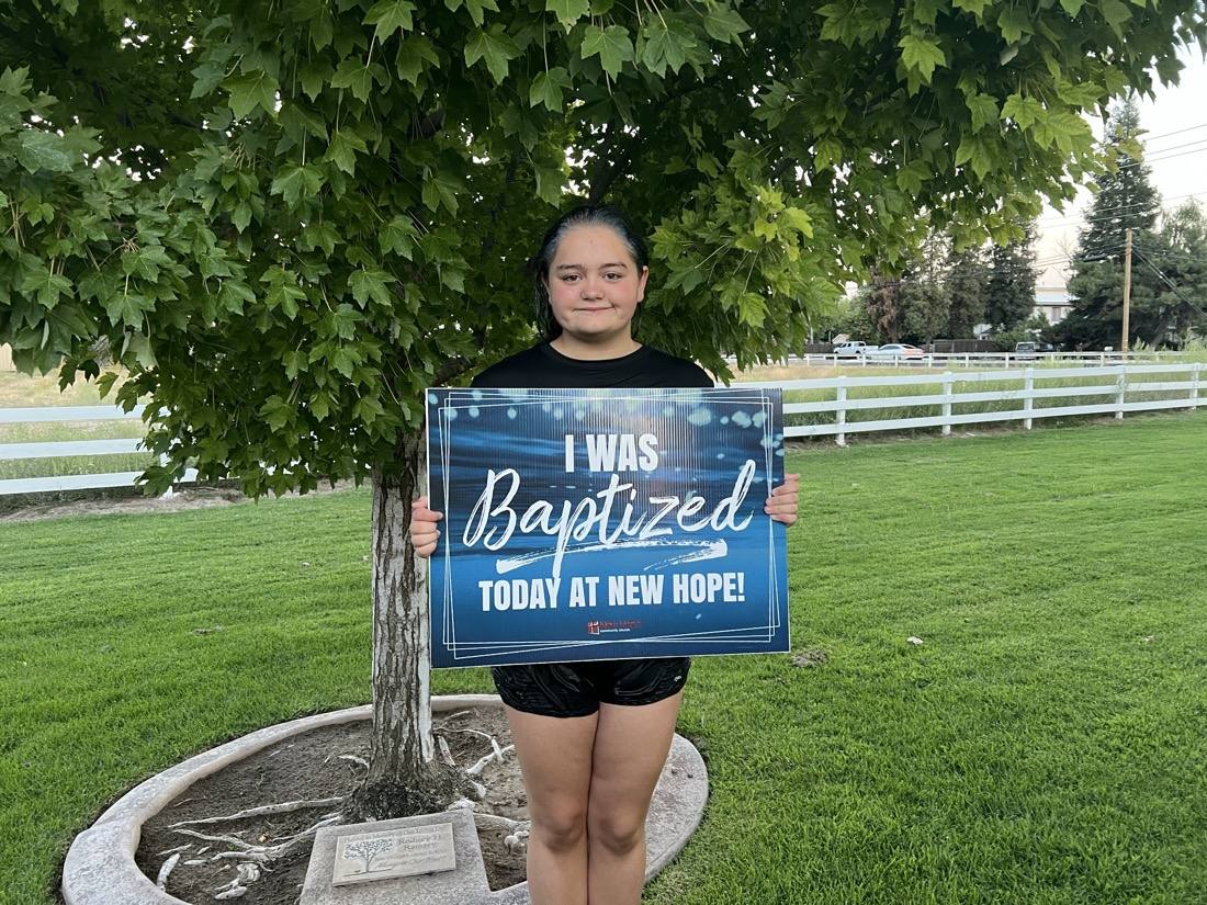 A New Hope member holding an I was baptized today sign on the church lawn