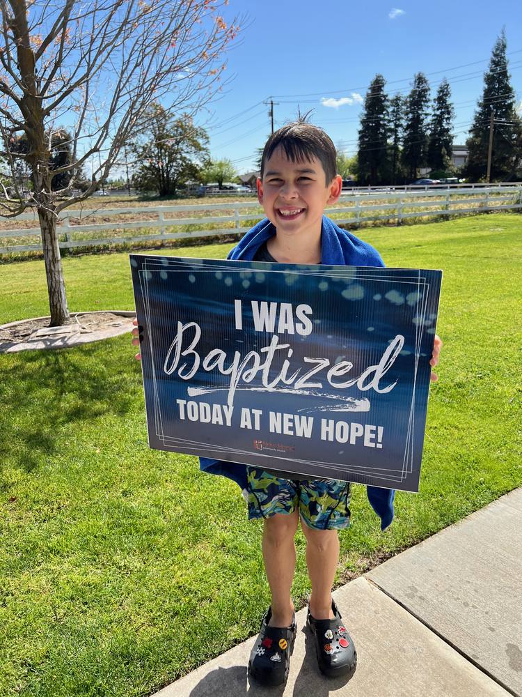 A young New Hope member holding an I was baptized today at New Hope sign on a sunny lawn