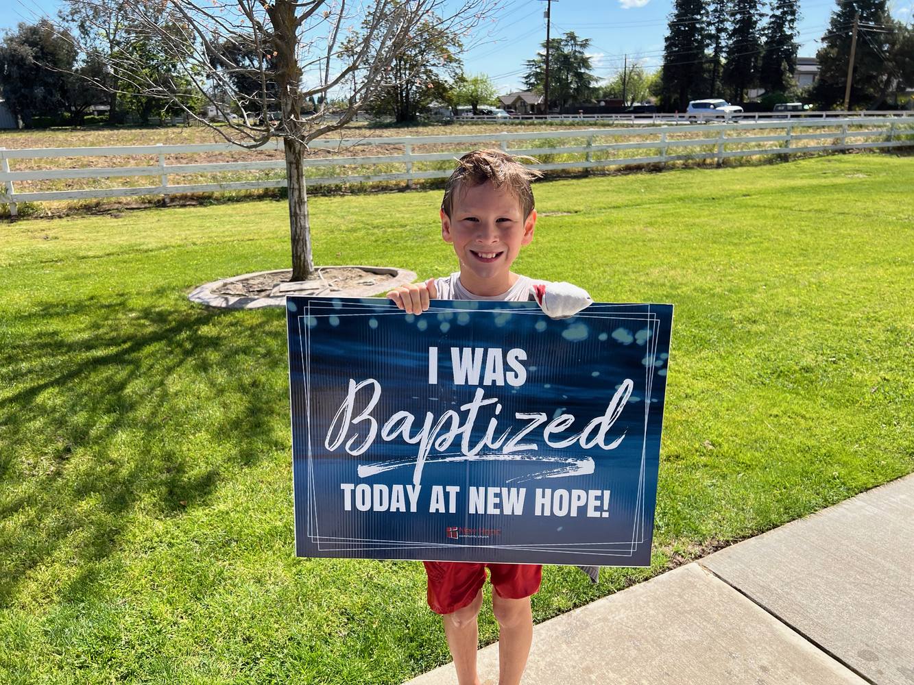A young New Hope member holding an I was baptized today at New Hope sign on a sunny lawn