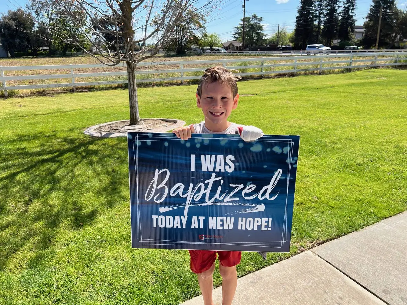 A young New Hope member holding an I was baptized today at New Hope sign on a sunny lawn