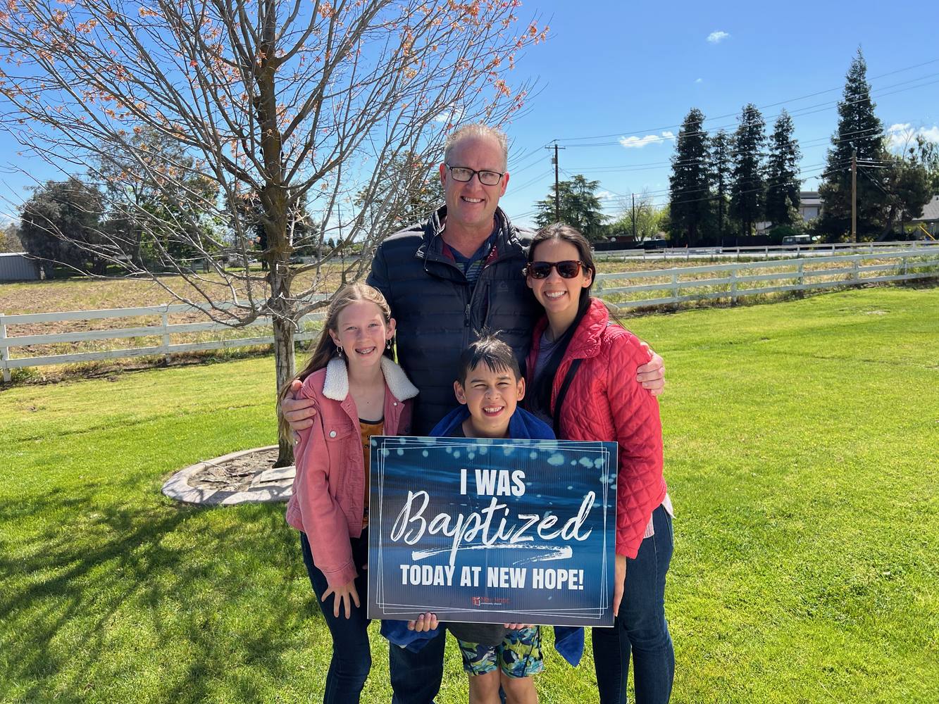 A New Hope family holding an I was baptized today at New Hope sign on a spring lawn