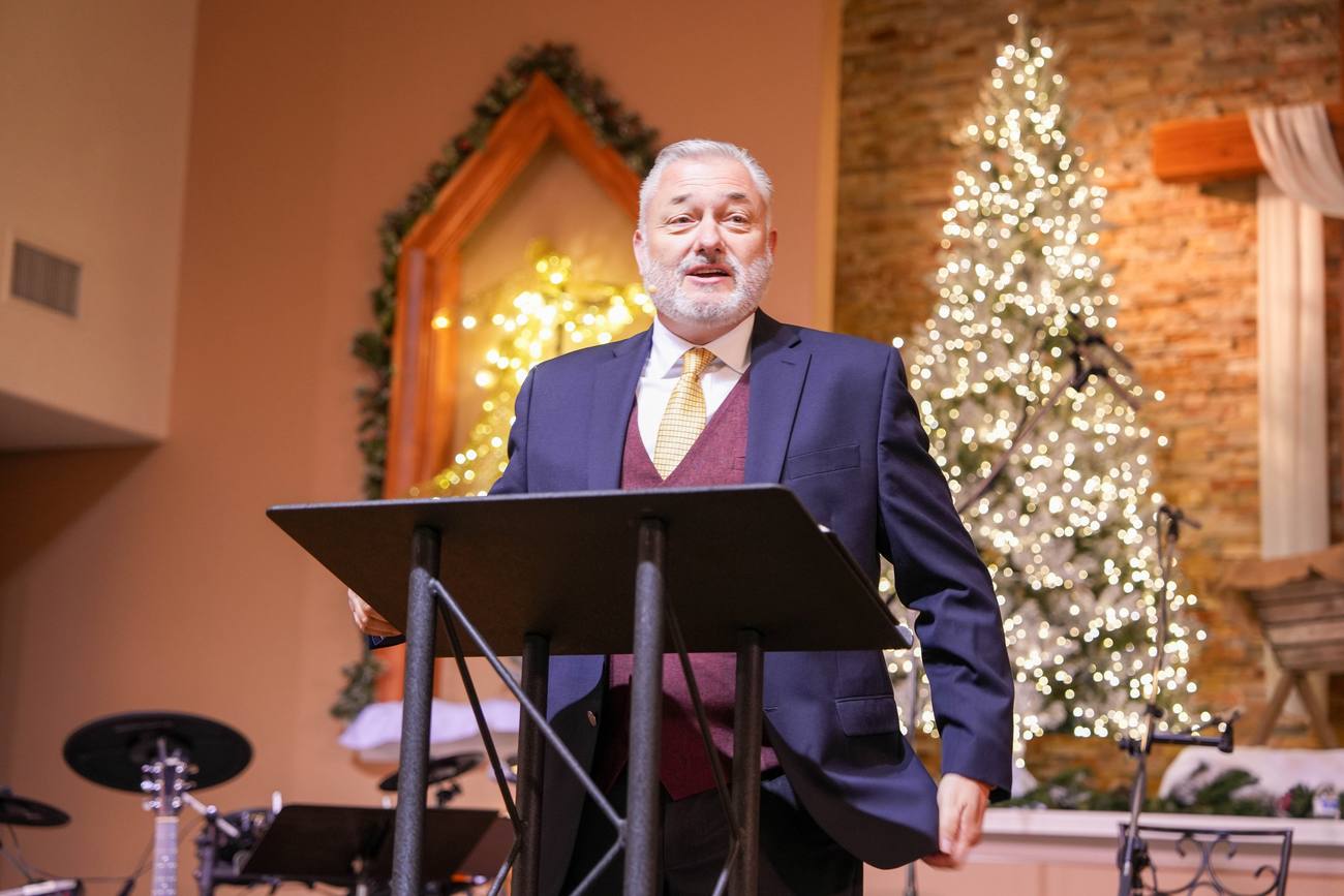 A pastor sharing a Christmas message at New Hope, a lit Christmas tree beside the stage