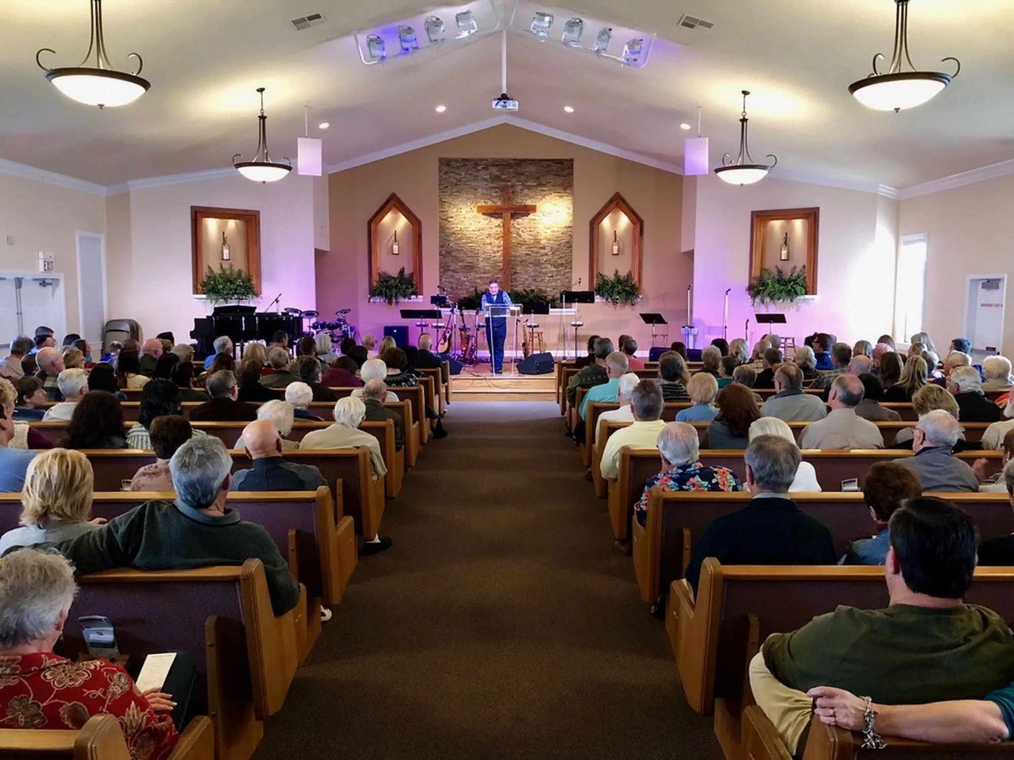 A full New Hope sanctuary during a Sunday service, with a pastor teaching from the lectern beneath the wooden cross
