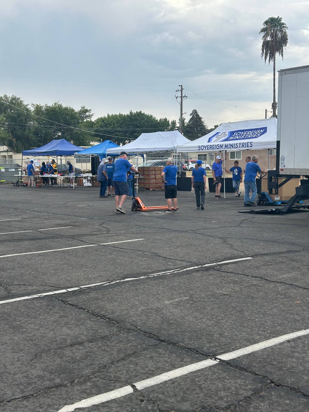 Volunteers in blue shirts setting up canopies beside the Sovereign Ministries box truck in a Calwa parking lot