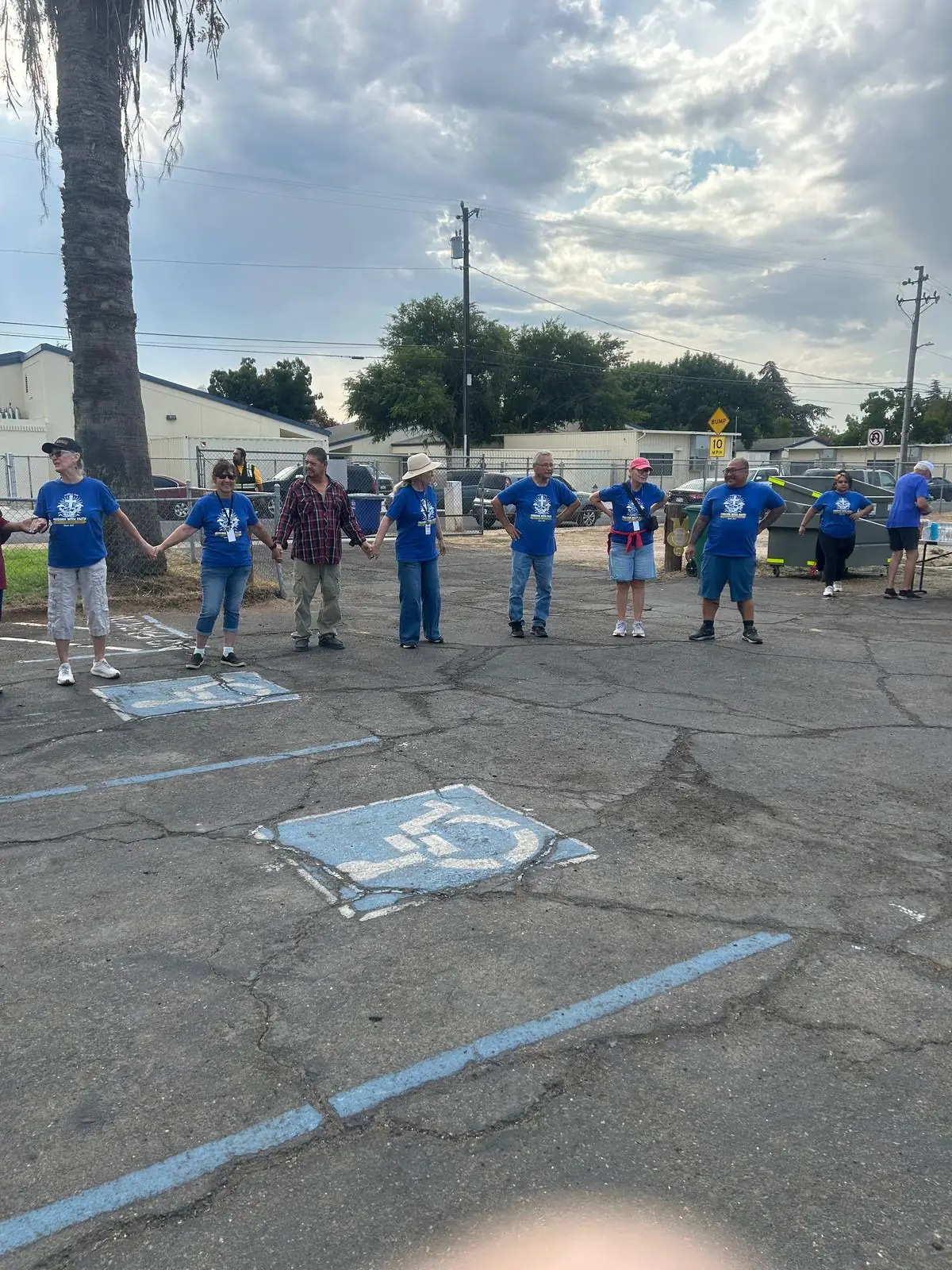 Volunteers standing in a wide circle holding hands in the parking lot before the morning starts