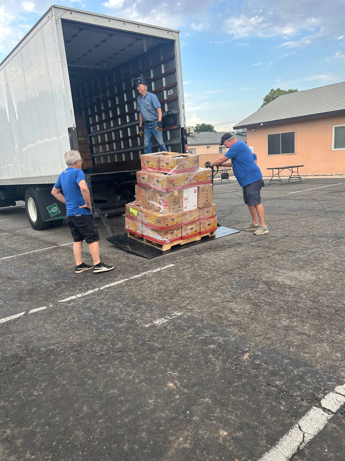 Two volunteers rolling a pallet of boxed food down the ramp of a box truck