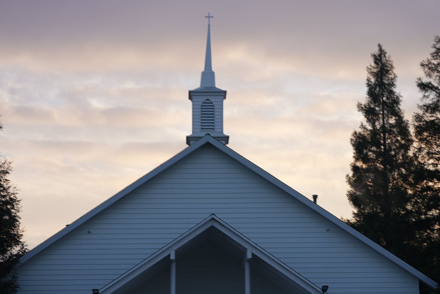 The steeple and cross of New Hope Community Church in Clovis against a dawn sky