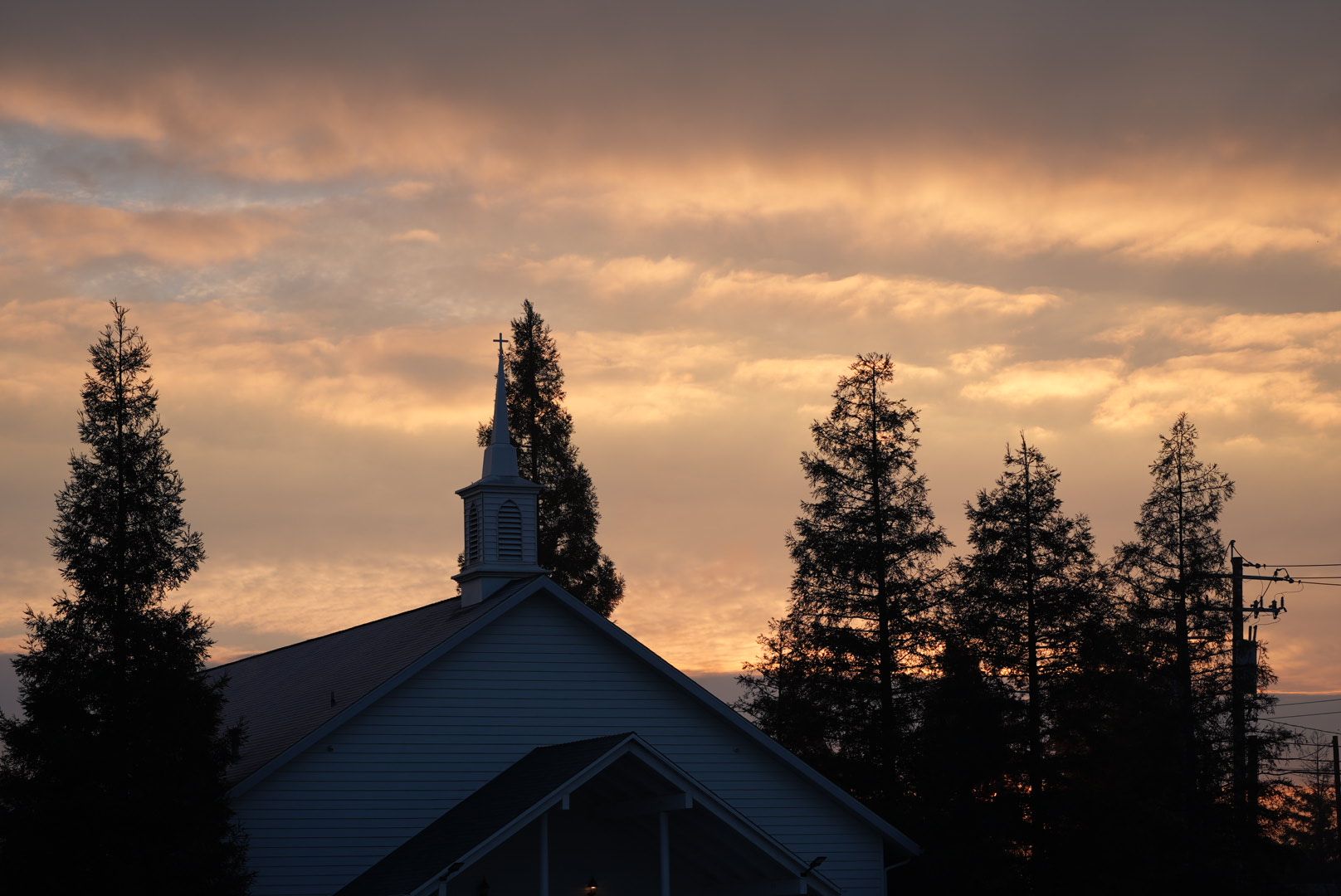 The New Hope steeple silhouetted against an orange sunrise, with tall pines around it