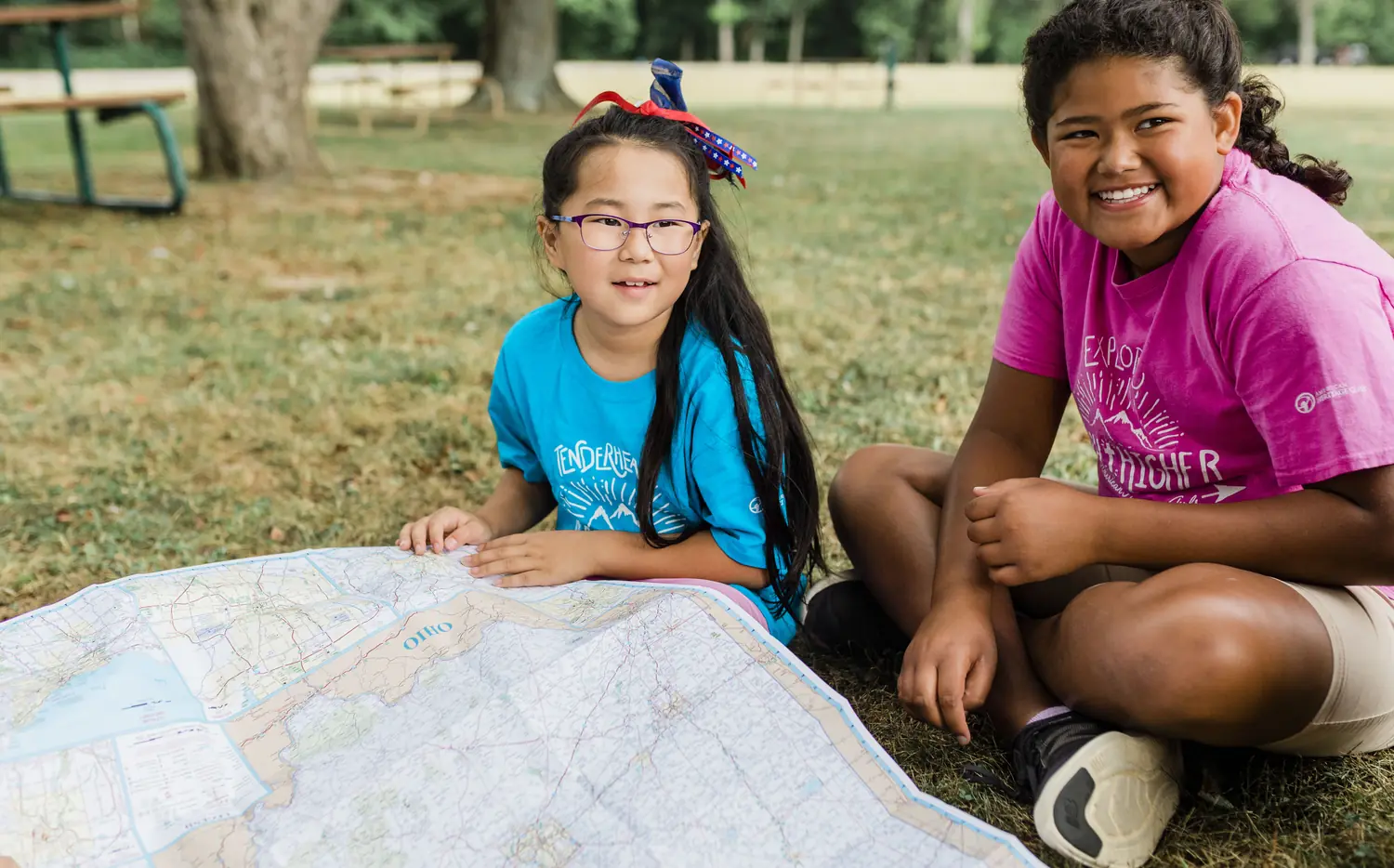 Two American Heritage Girls reading a topographic map together on the grass