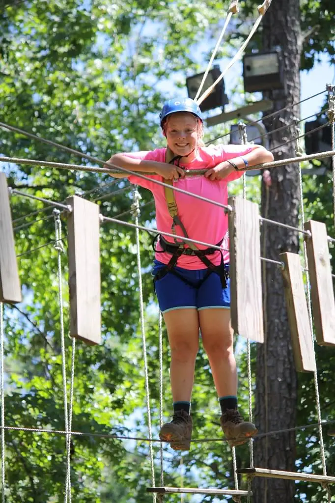 An American Heritage Girl crossing a high ropes bridge in a harness