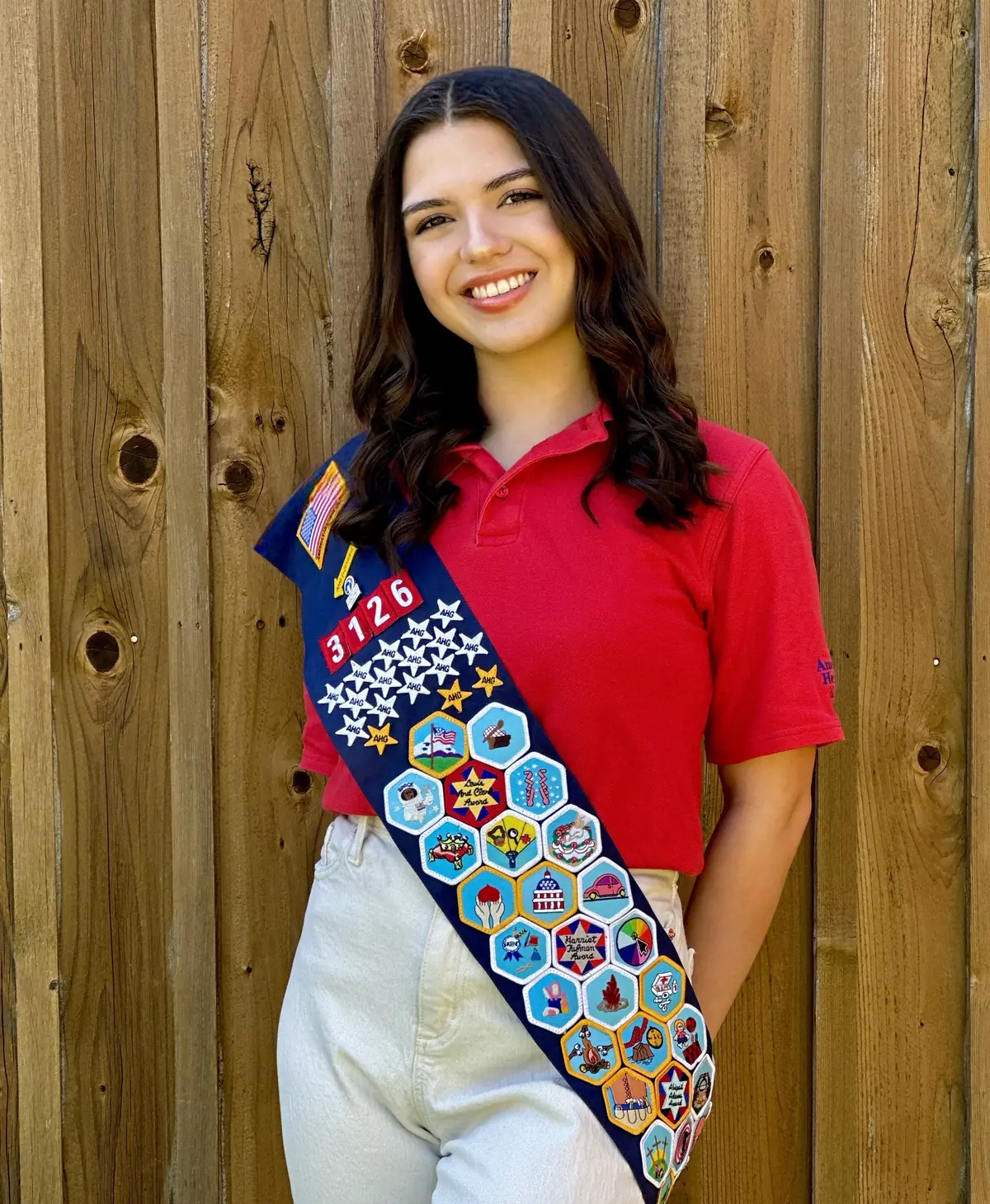 A Patriot-level American Heritage Girl wearing a sash filled with earned badges