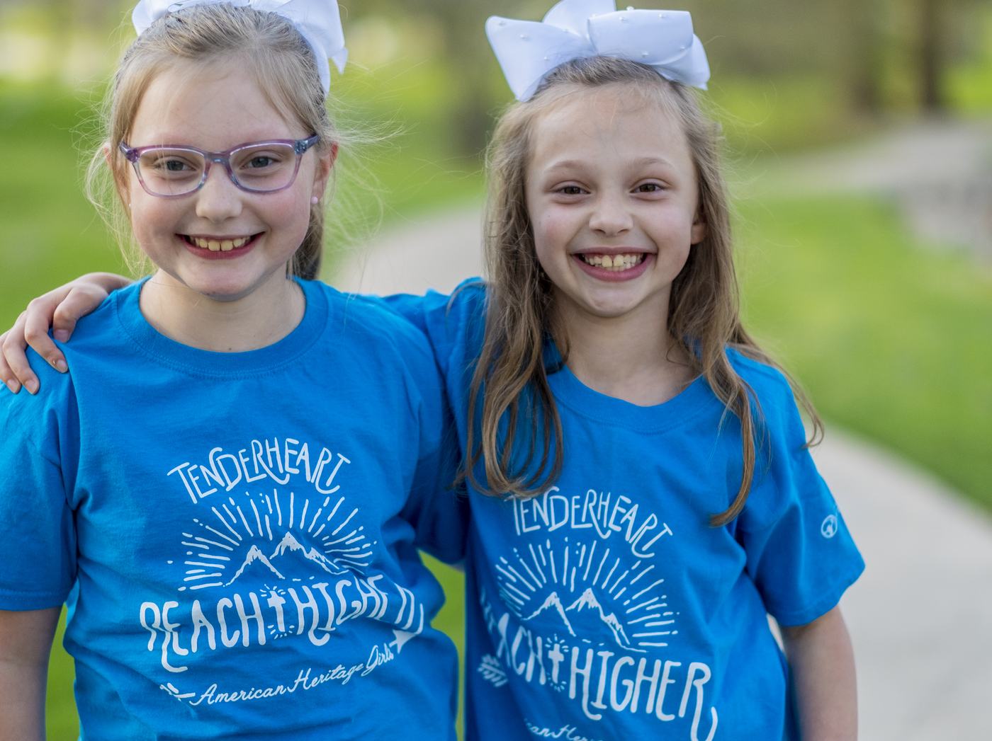 Two American Heritage Girls in troop t-shirts with their arms around each other