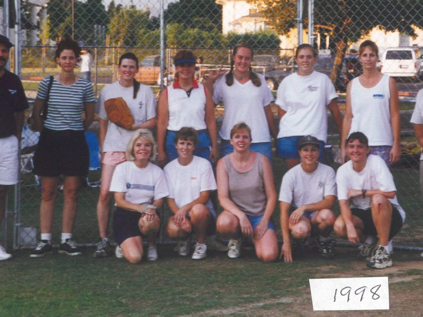 A New Hope church softball team posed at the ballfield fence in 1998, the year handwritten on a card at their feet