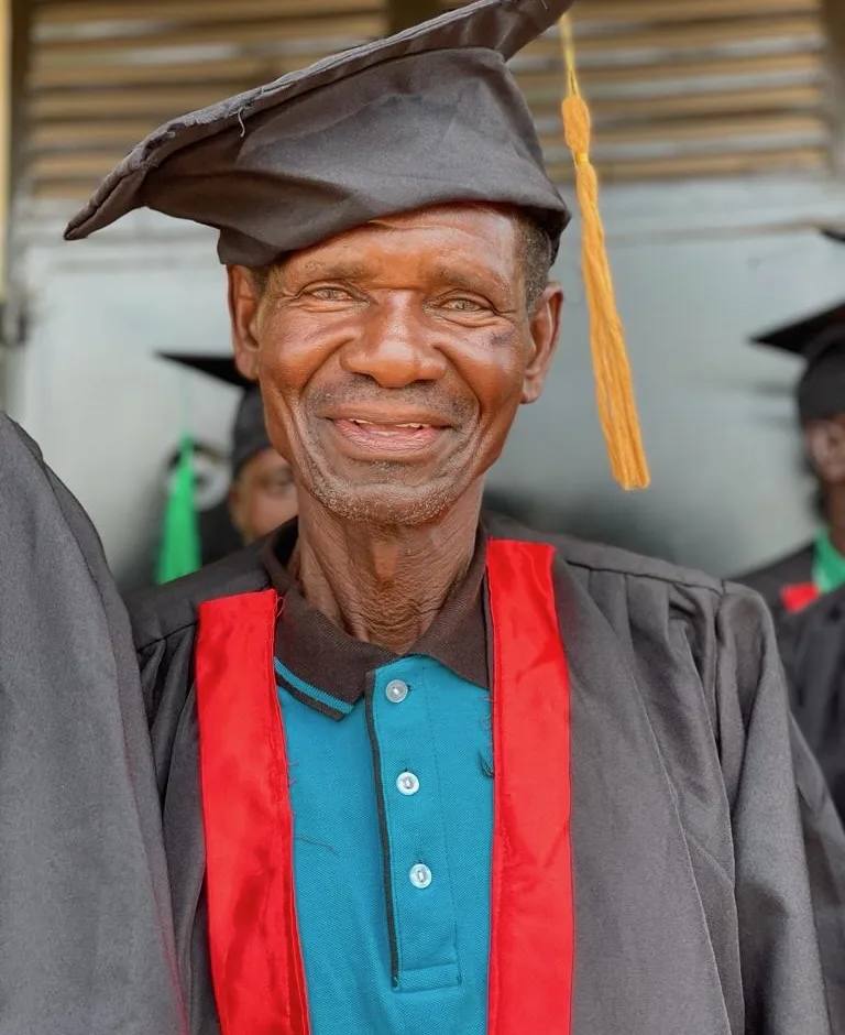 A smiling pastor in a graduation cap and gown with a red stole.