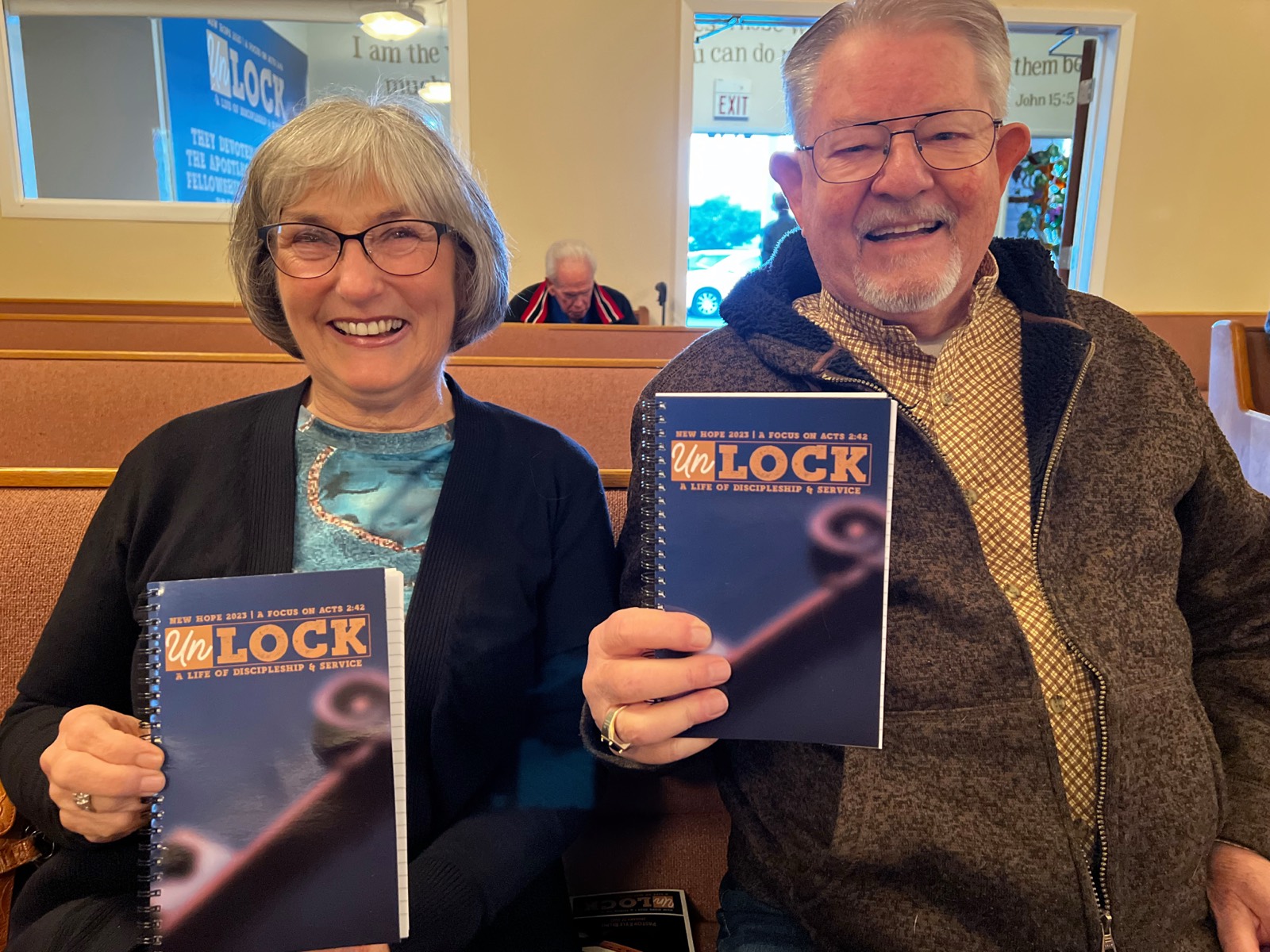 A couple from New Hope smiling in the sanctuary, holding their New Hope UnLock study guides on discipleship and service