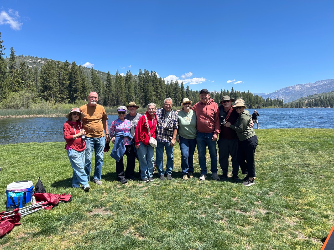 A group of Ignite Marriage Ministry couples posed together on the grass at Hume Lake, with the lake and pine-covered mountains behind them