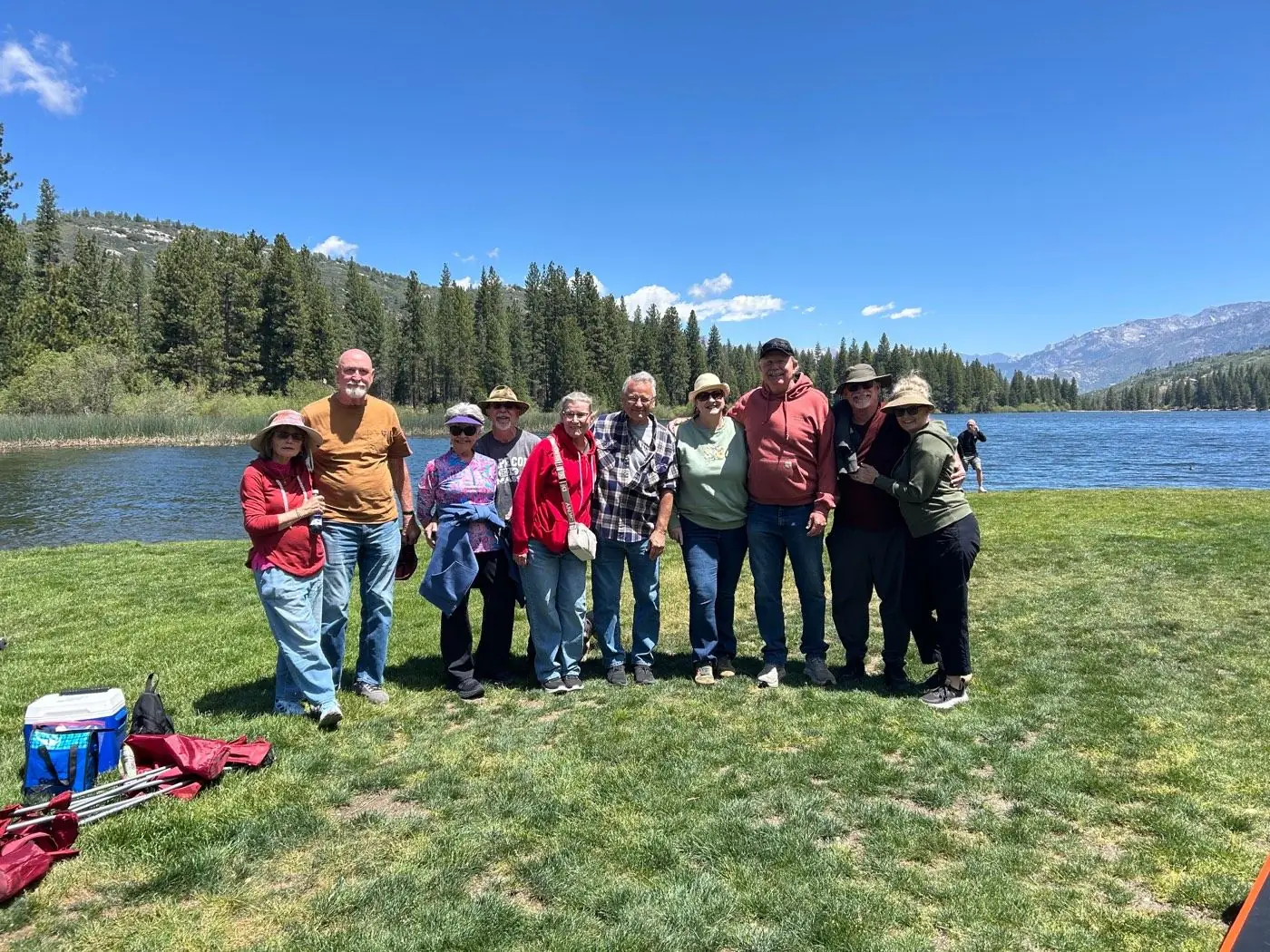 A group of Ignite Marriage Ministry couples posed together on the grass at Hume Lake, with the lake and pine-covered mountains behind them