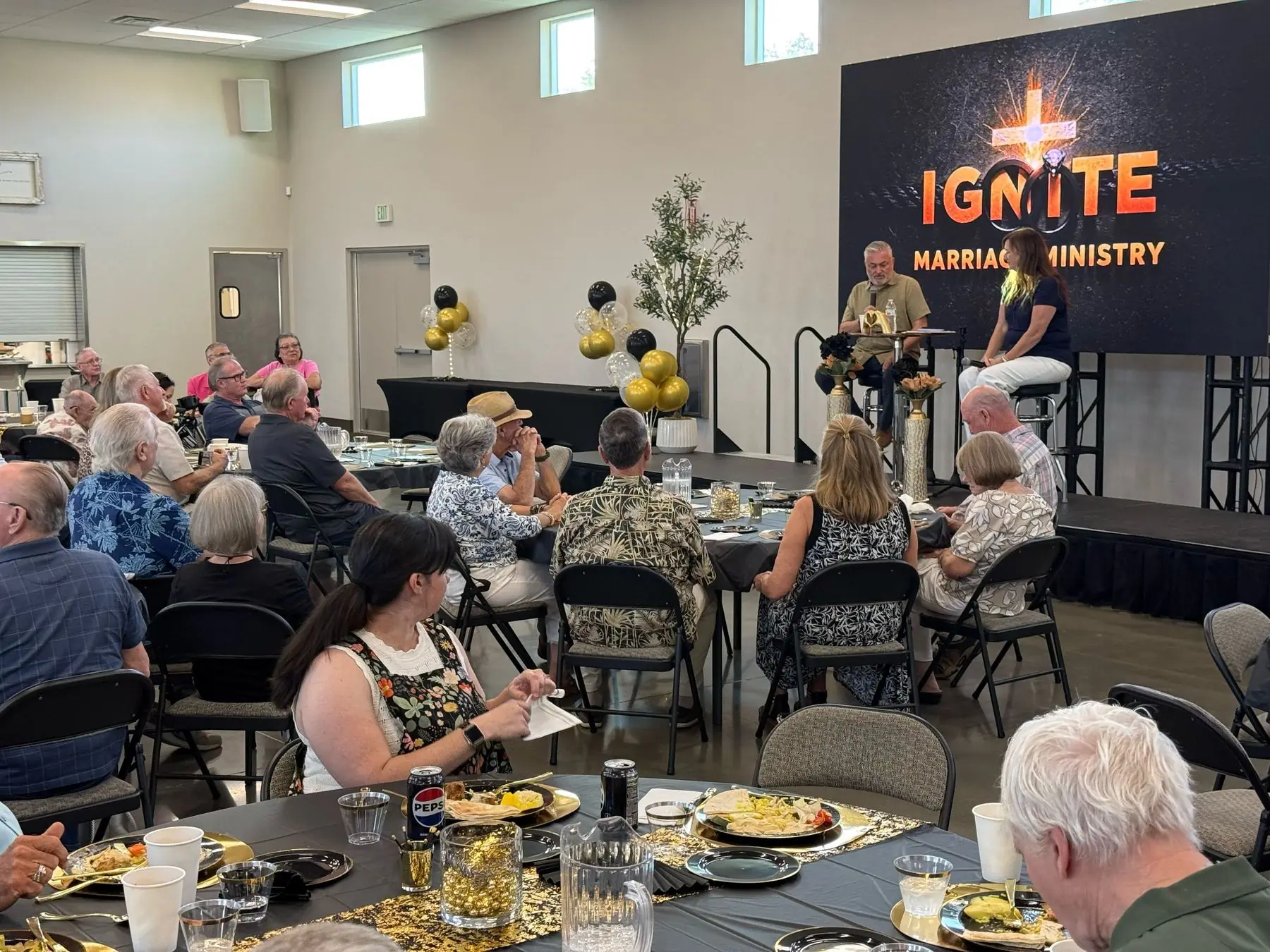 Couples seated at dinner tables watching a speaker on stage beneath the Ignite Marriage Ministry banner