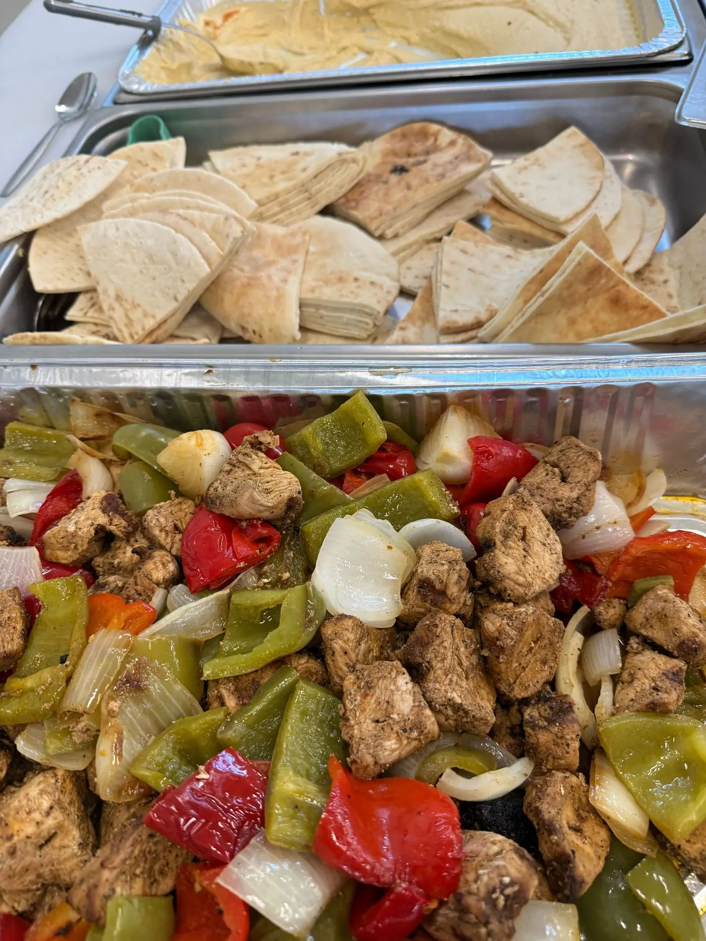 A catering tray of grilled chicken, peppers, and onions with warm pita