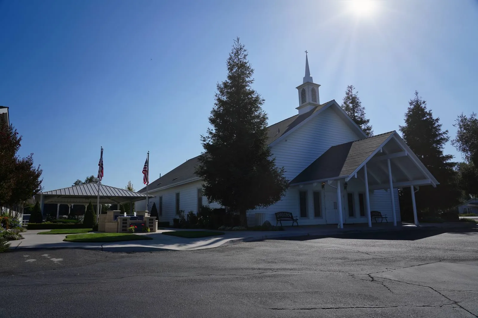 New Hope's white sanctuary in Clovis, its steeple and cross against a clear sky, with two flagpoles and a covered patio beside the empty parking lot
