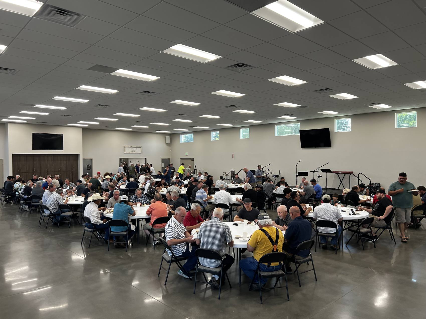 A hall full of men of New Hope seated at tables together for the annual Men's BBQ