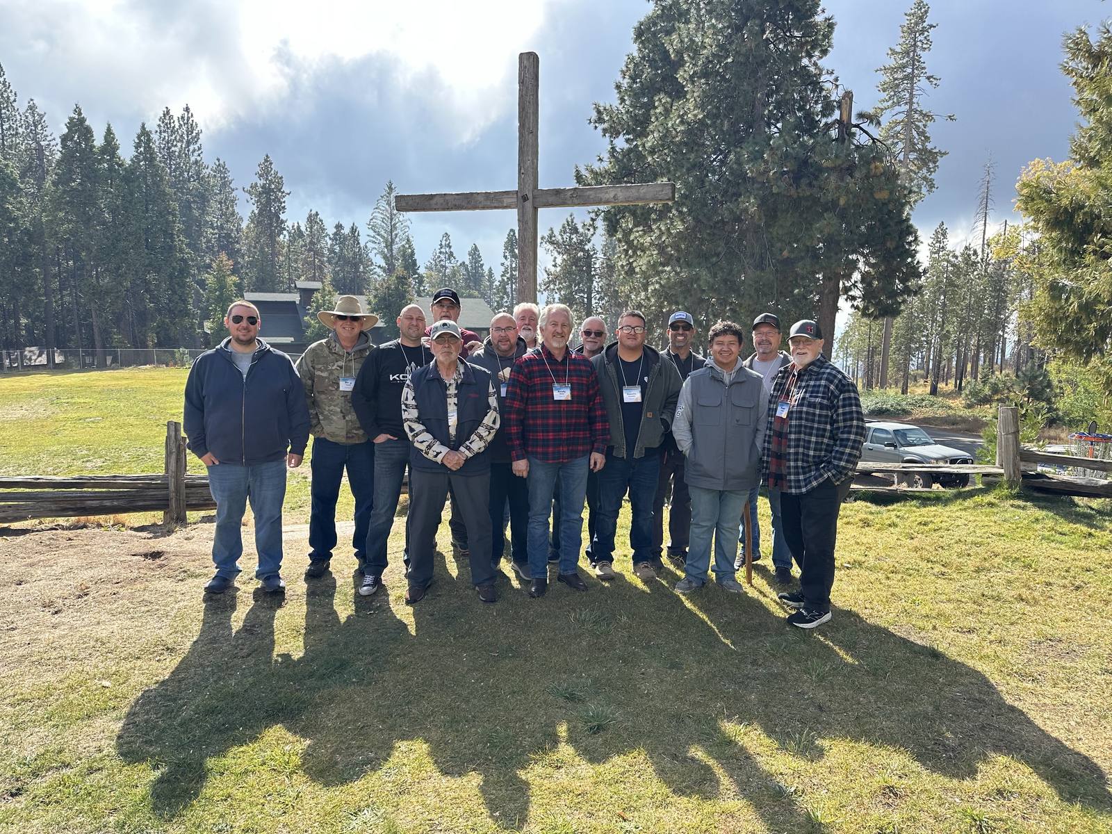 Men of New Hope gathered together by the wooden cross at Man Camp in the pines