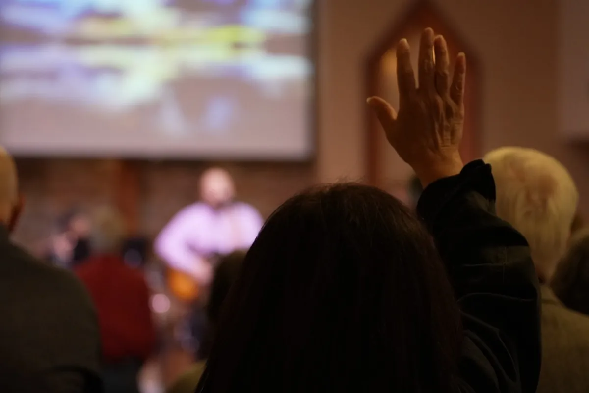 A New Hope worshipper with hand raised during a service, projection screen visible in the background