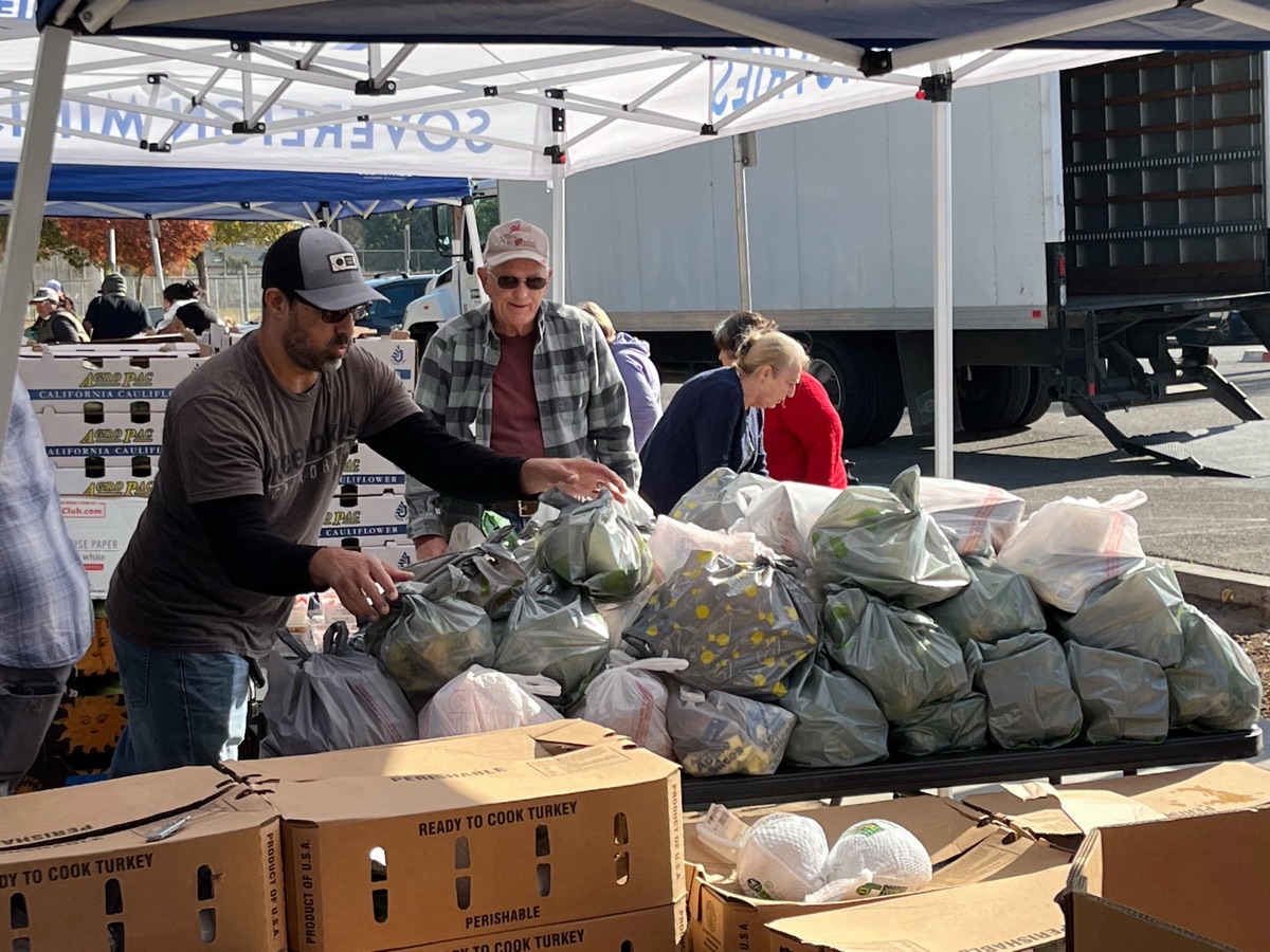 Volunteers reaching for bagged produce on a long table piled with grocery bags ready to hand out