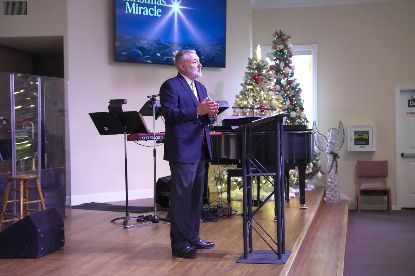 A pastor speaking from the stage beside a decorated Christmas tree at a New Hope service