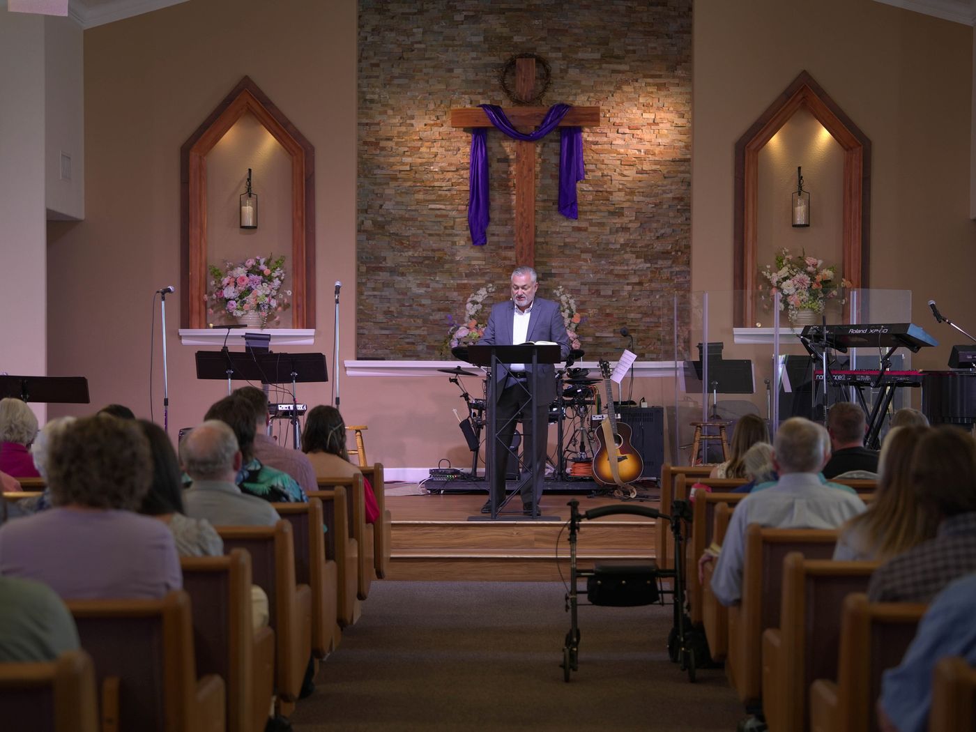 A pastor preaching from the sanctuary stage beside a purple-draped cross on Easter Sunday in Clovis