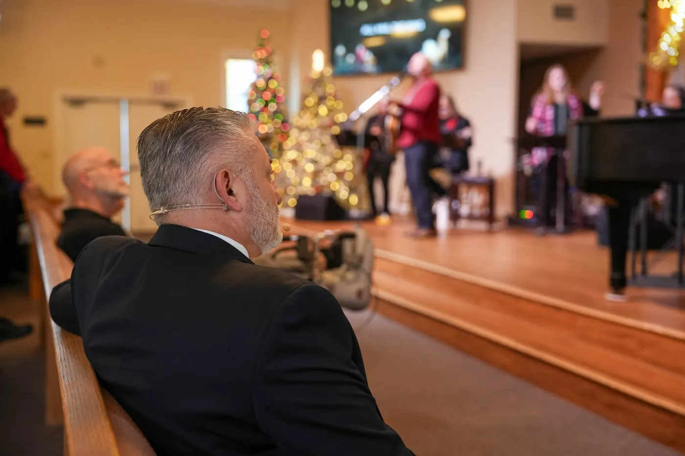 A man watching from a pew while the worship team plays at a New Hope Christmas service, lit trees on the platform