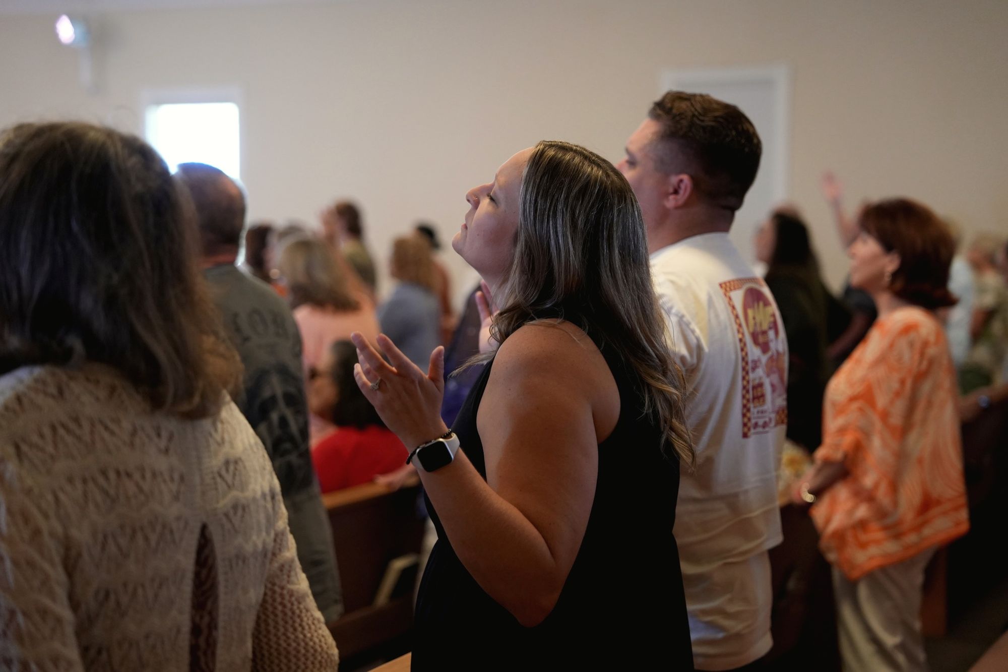 A woman standing with the congregation during Sunday worship, her face lifted and one hand raised, others singing around her