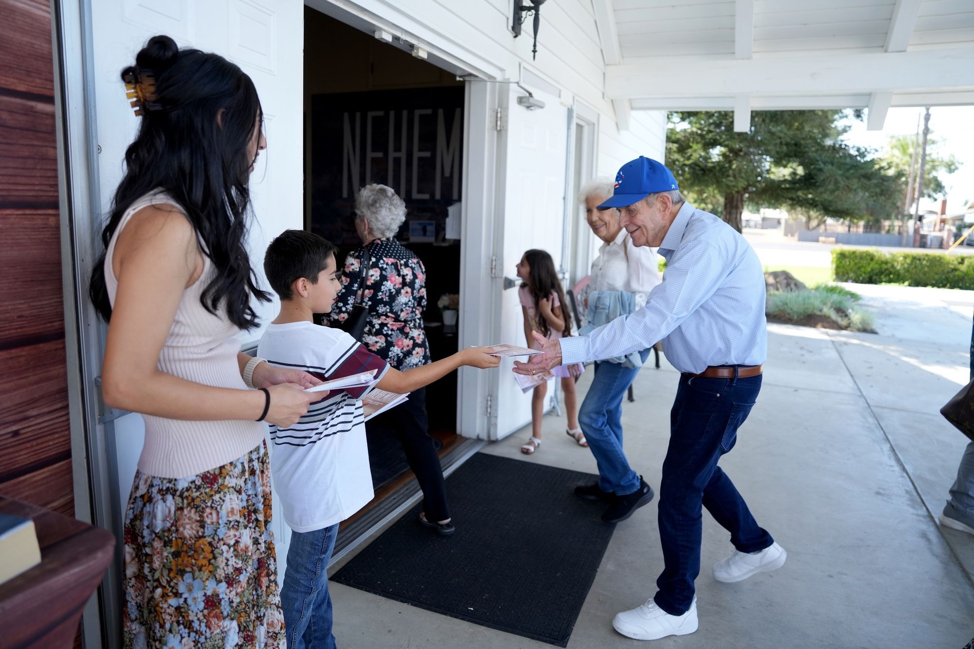 A greeter shaking hands with an arriving couple while a boy hands out bulletins at the New Hope entrance