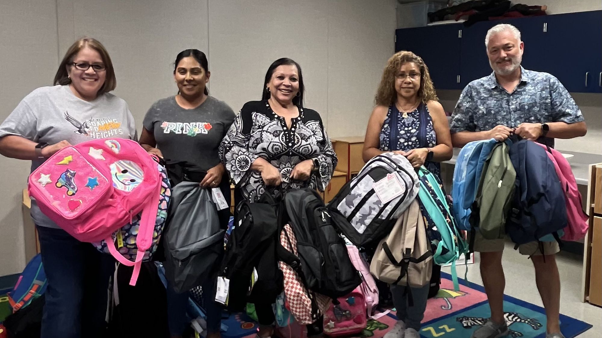 Volunteers holding armfuls of backpacks gathered for a Helping Hands service project