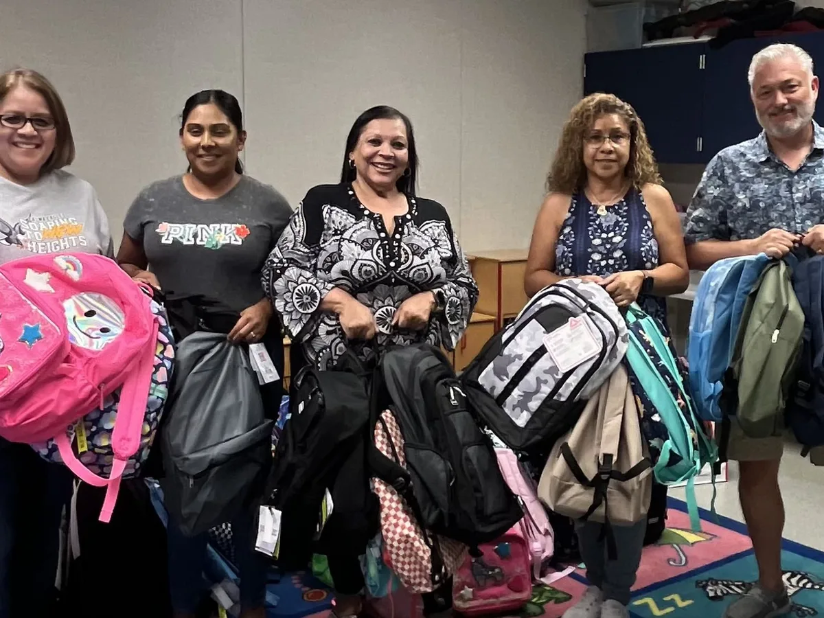 Five volunteers smile as they hold armfuls of donated backpacks.