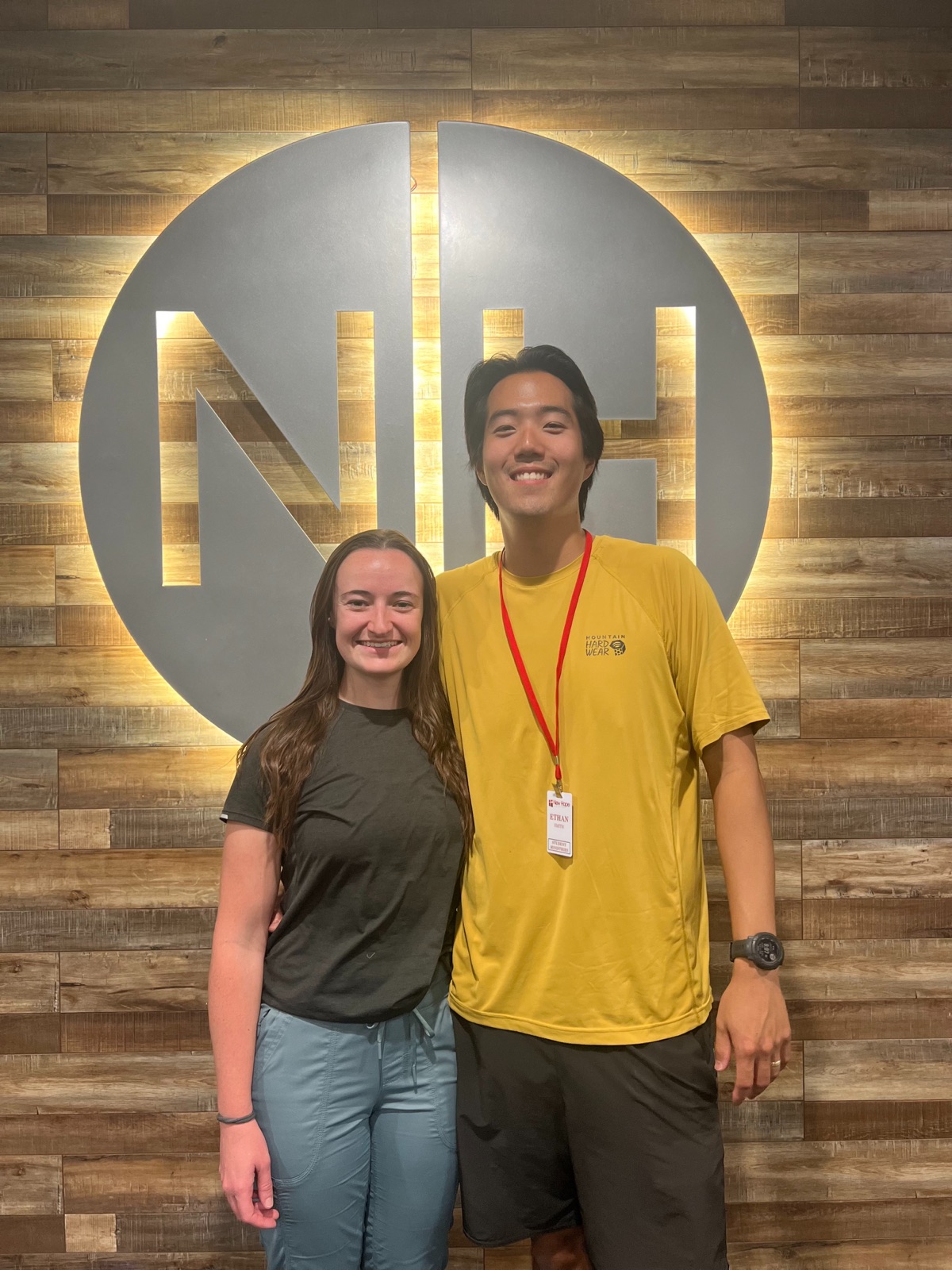 Ethan and a Student Ministries co-leader standing in front of the New Hope wall logo at Hume Lake camp