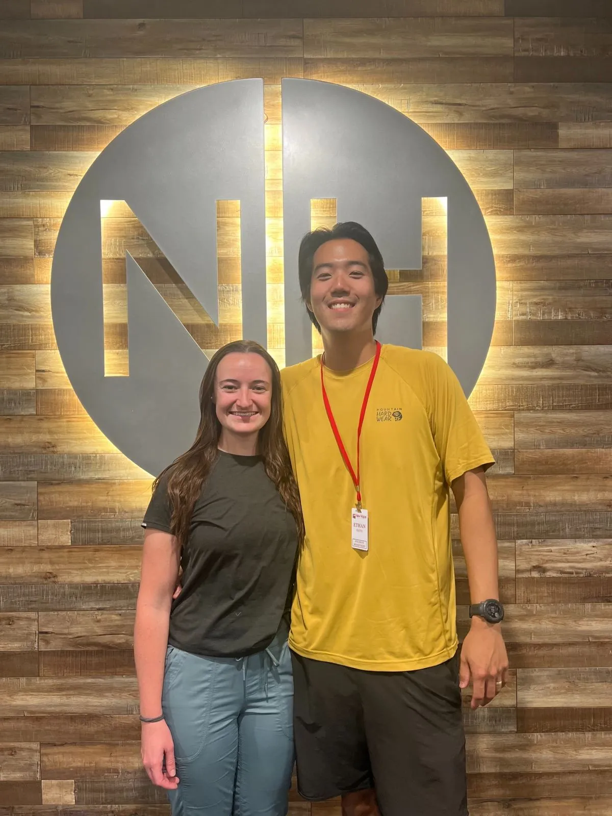 Ethan and a Student Ministries co-leader standing in front of the New Hope wall logo at Hume Lake camp