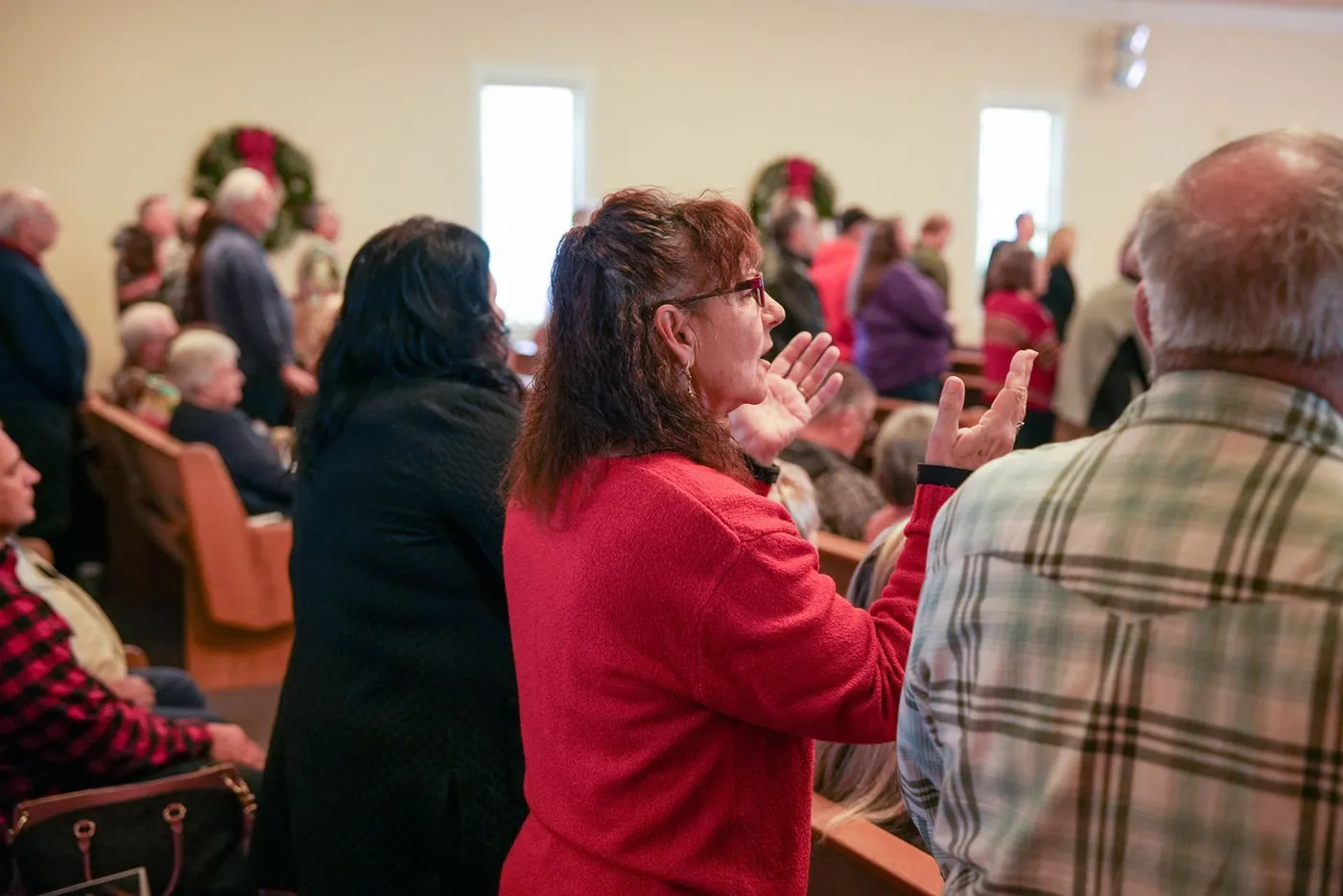 People standing and singing at a New Hope Christmas service, a woman in red with both hands raised