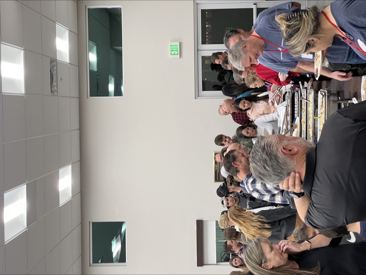 A mixed-age crowd lined up at a long buffet table of chafing dishes in the New Hope fellowship hall, filling their plates