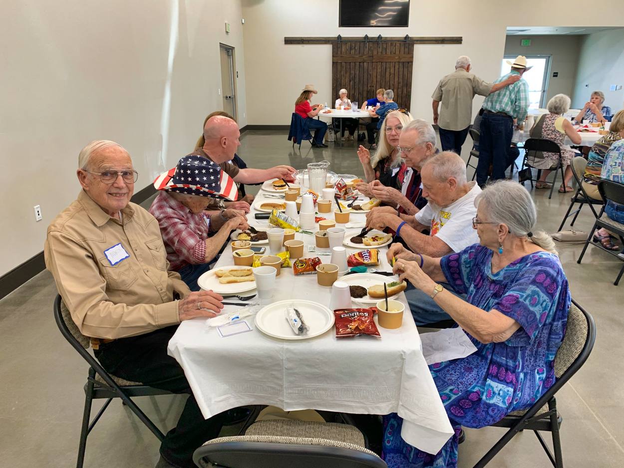 Several New Hope members seated along a long white table sharing a meal together in Clovis, plates and red napkins in front of them