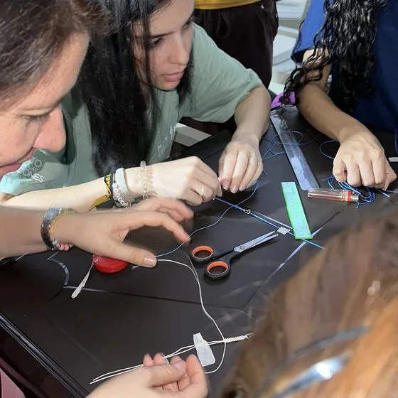 Hands at a dark worktable with scissors, thread and a ruler during a craft class.