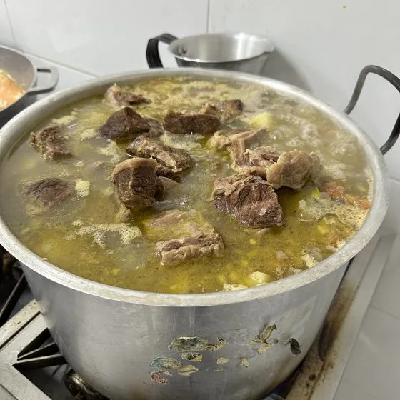 A large pot of soup with chunks of beef, cooking for the weekly meal.