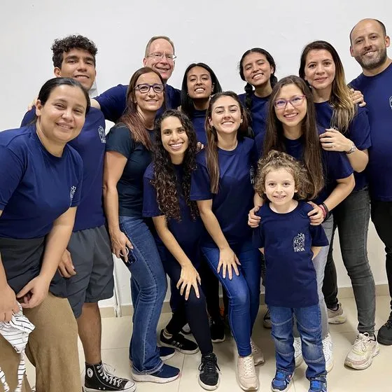 A smiling group in matching navy shirts stands together indoors.