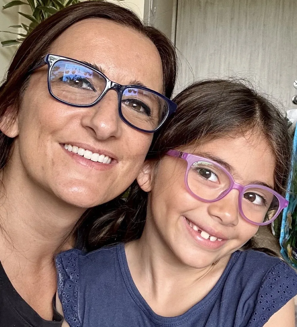 Rebekah Slick smiling in blue glasses beside a smiling girl in purple glasses.