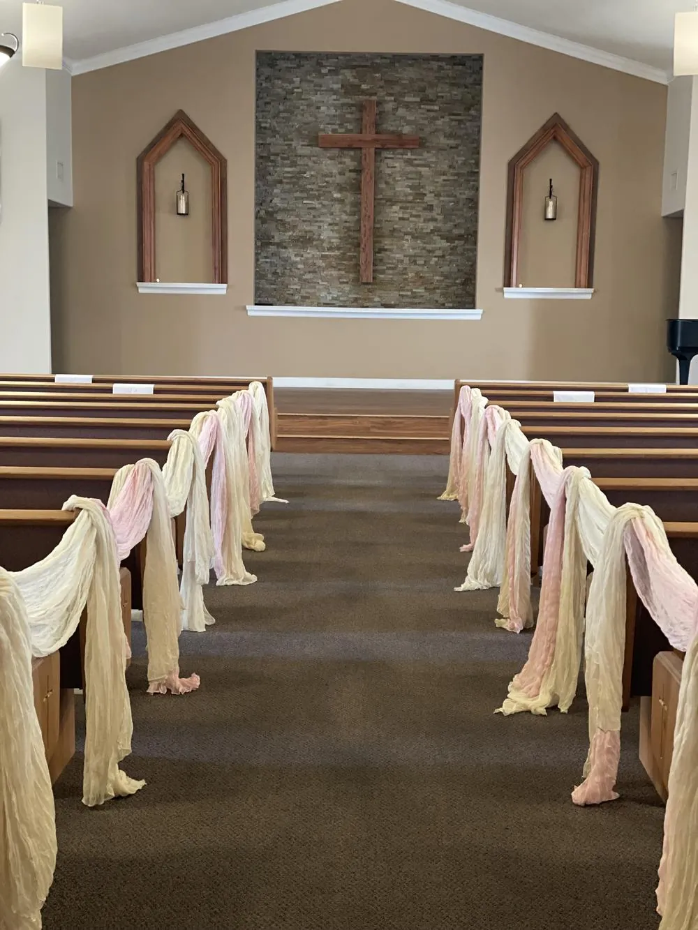 Sanctuary aisle draped in cream and blush fabric, leading to the wooden cross on the stone wall