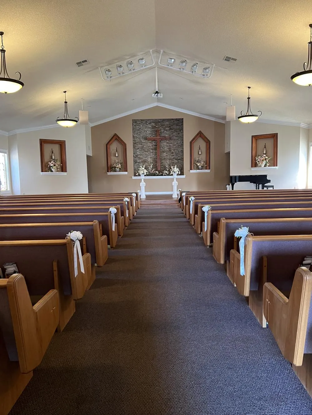 Wide view of the decorated sanctuary, pews with white ribbons and the piano at the front