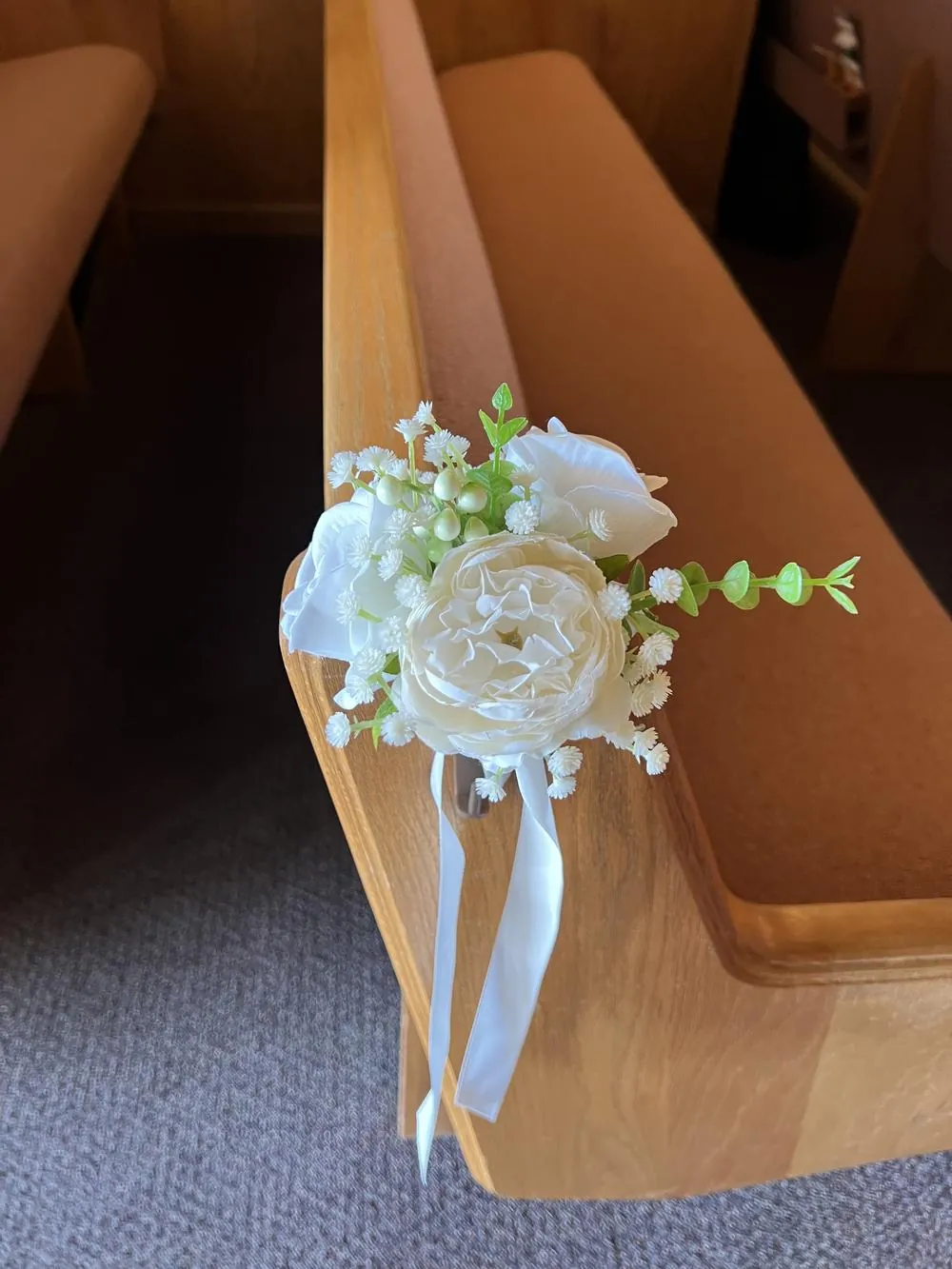 White and cream flowers with trailing ribbon on the end of a wooden pew