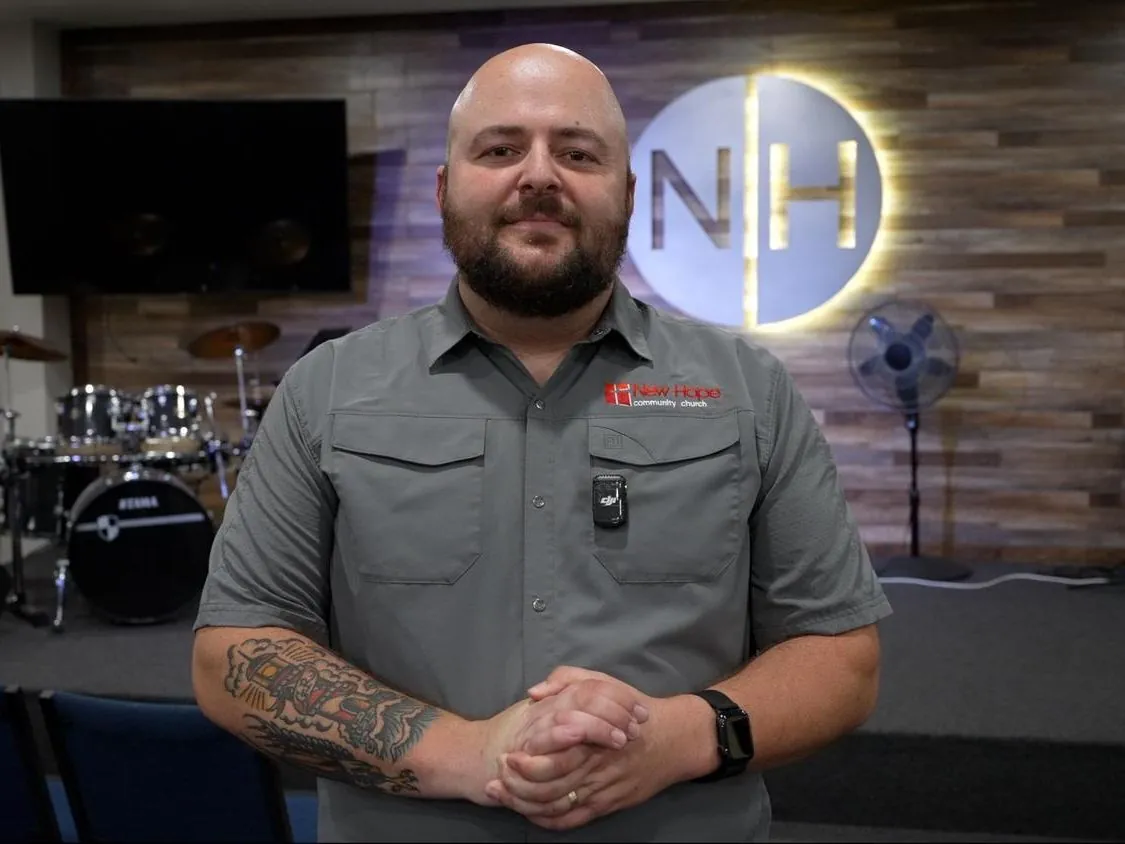 A New Hope young adult ministry leader standing in the Bridge, the lit NH monogram on the wall behind him